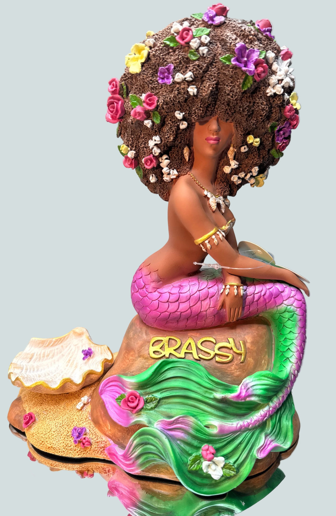 Original Brassy Black Afro mermaid statue from the Oshún Dynasea, featuring a floral afro, pink and green tail, seashell jewelry, and handcrafted fantasy details.
