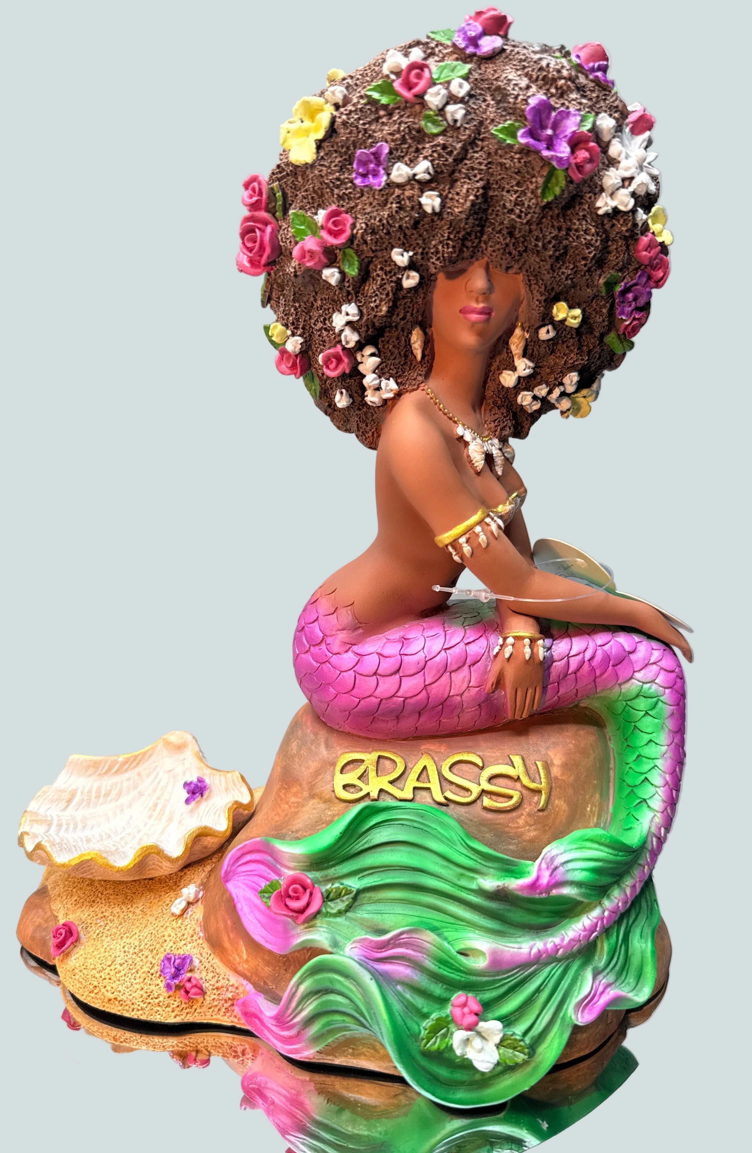 Original Brassy Black Afro mermaid statue from the Oshún Dynasea, featuring a floral afro, pink and green tail, seashell jewelry, and handcrafted fantasy details.