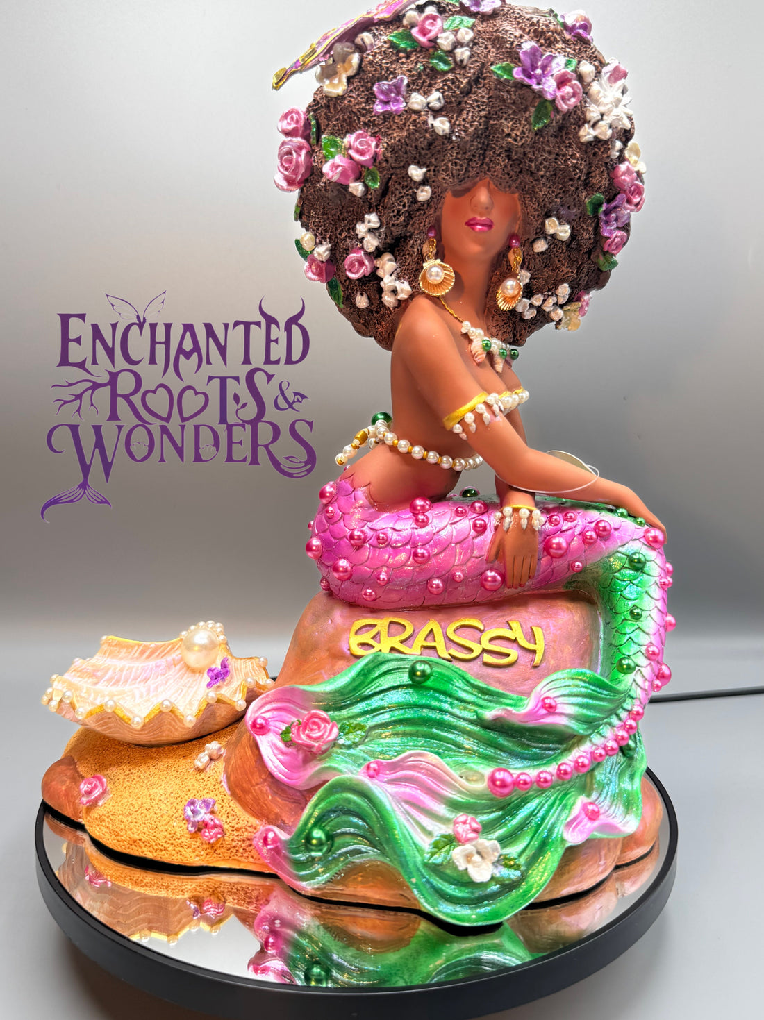 Penda Lú, a Black mermaid with rich brown skin, a shimmering pink and green mermaid tail adorned with pearls. A one-of-a-kind Afro Mermaid fantasy statue celebrating Black mermaids, magical artistry, and inclusive fantasy.