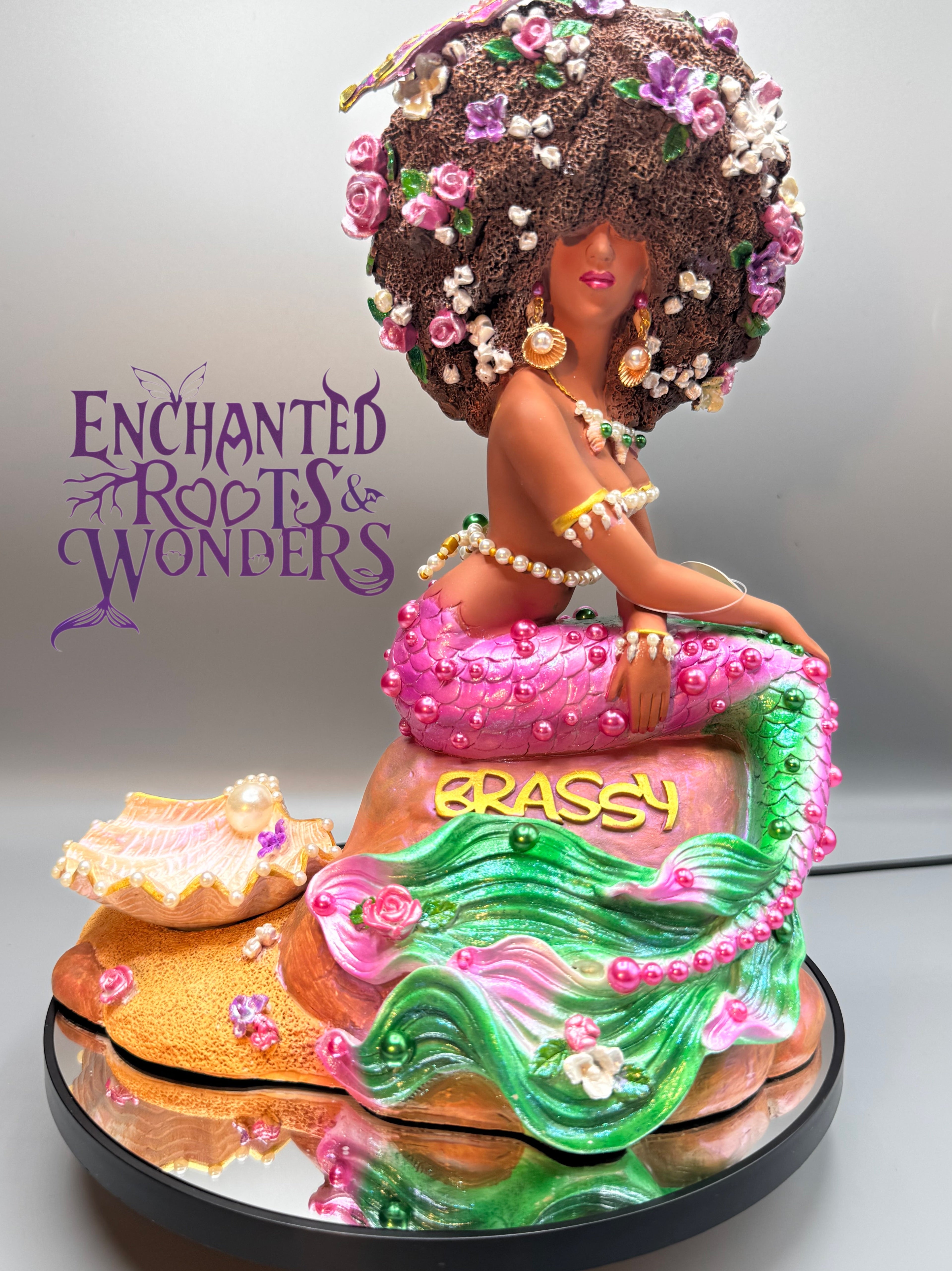 Penda Lú, a Black mermaid with rich brown skin, a shimmering pink and green mermaid tail adorned with pearls. A one-of-a-kind Afro Mermaid fantasy statue celebrating Black mermaids, magical artistry, and inclusive fantasy.