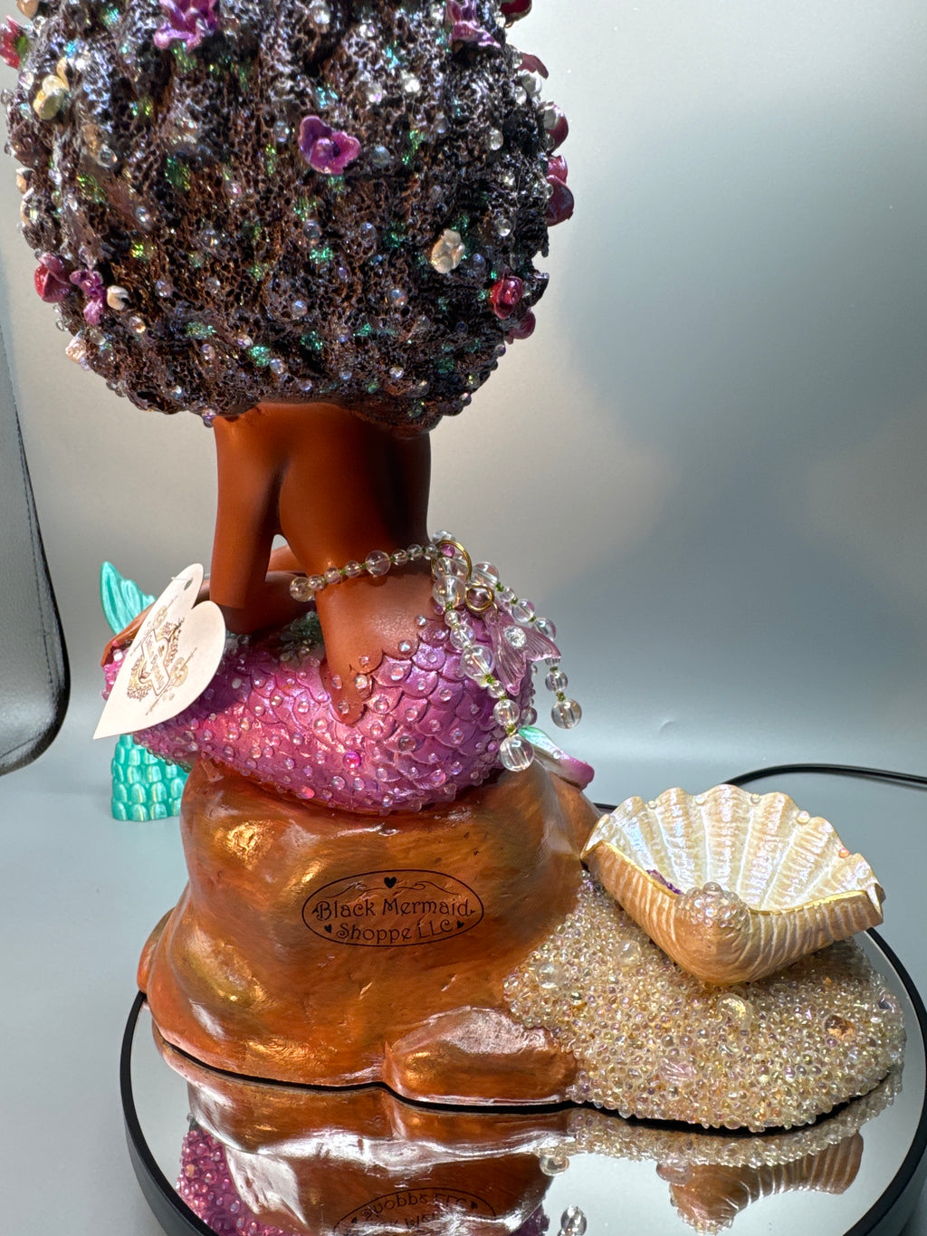 Rear view of the Lumira Brassy figurine showing her lustrous tail, pearl embellishments, and voluminous flower-filled hair cascading down her back. Glossy finish and elegant sculpting.