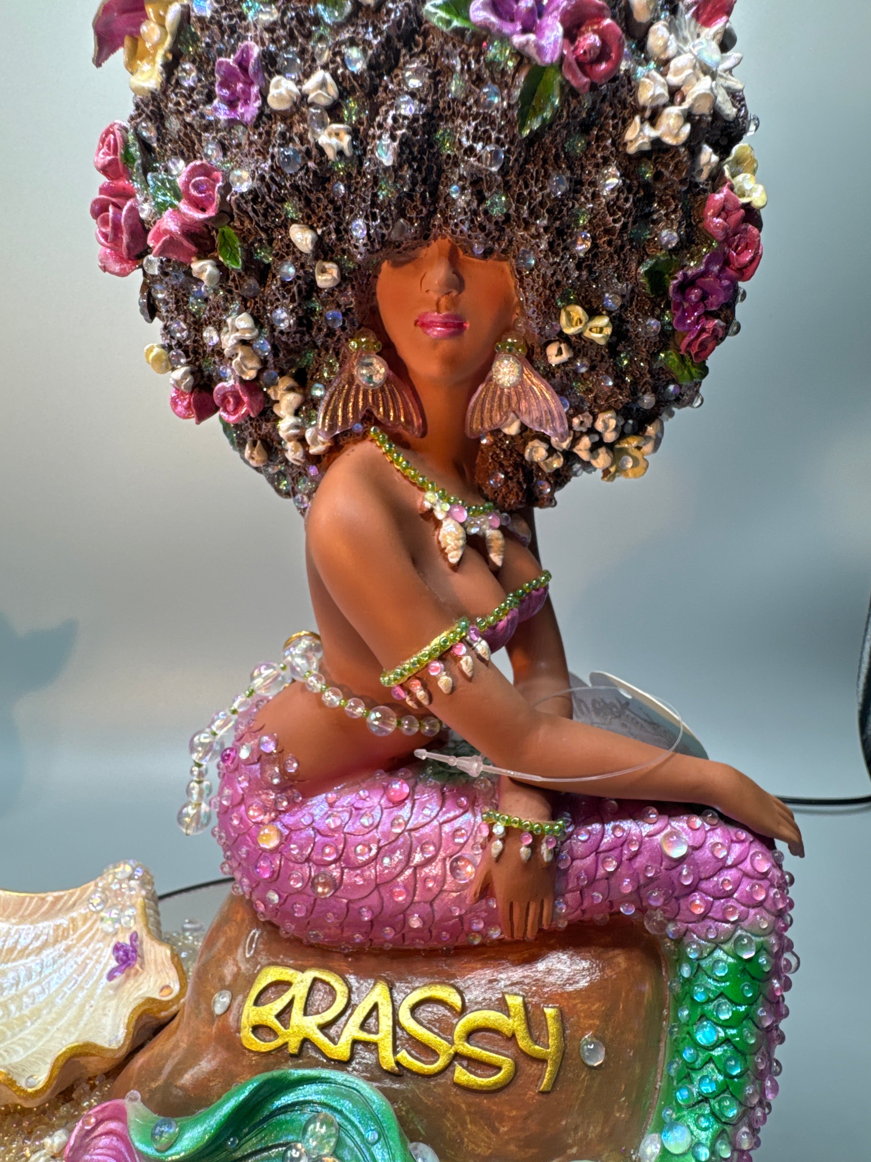 Close-up of hand-painted Lumira mermaid figurine showing a shimmering pearlescent shell surrounded by sparkling rocks and seafoam-colored details. An original Brassy statue by Clover Jené Mermaid.