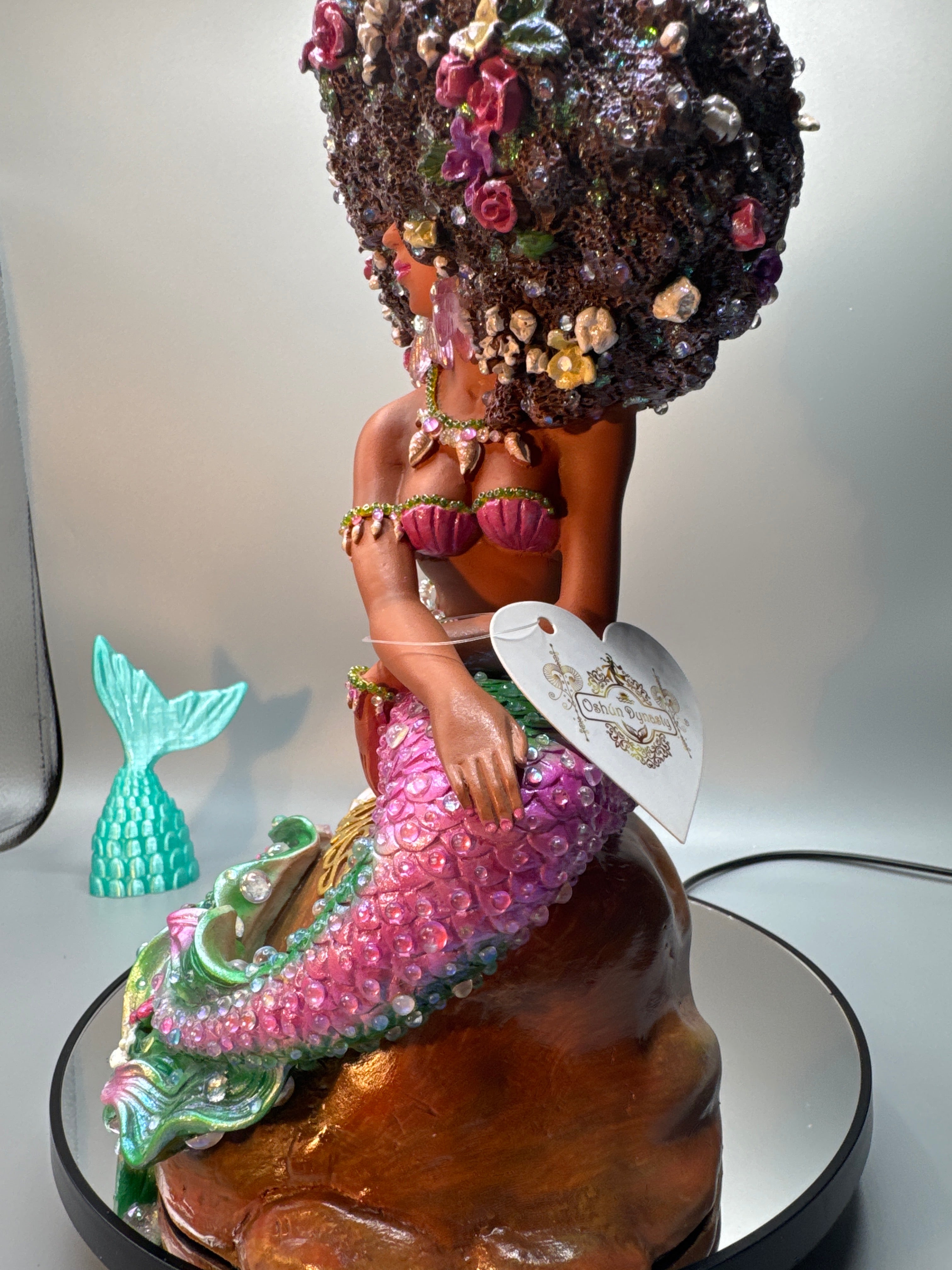 Side view of Lumira Brassy mermaid figurine highlighting her jeweled necklace, shell-inspired top, and detailed tail scales adorned with glossy bubbles. Hand-painted Black mermaid art by Clover Jené Mermaid.