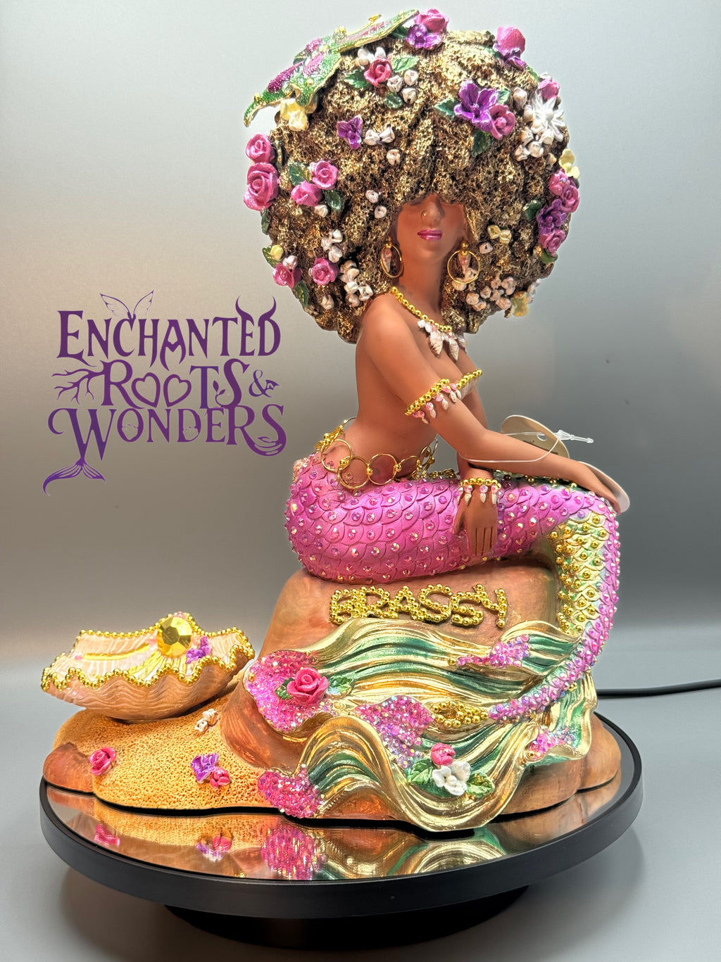Afro mermaid statue with pink and gold rhinestone tail, hoop earrings, and bold Afro hairstyle. One-of-a-kind Brassy from the Oshún Dynasea collection. Inspired by a round-the-way NYC goddess energy, Luxey Lo brings regal street charm and divine mermaid magic. Handmade Black mermaid fantasy art by Clover Jené Mermaid.