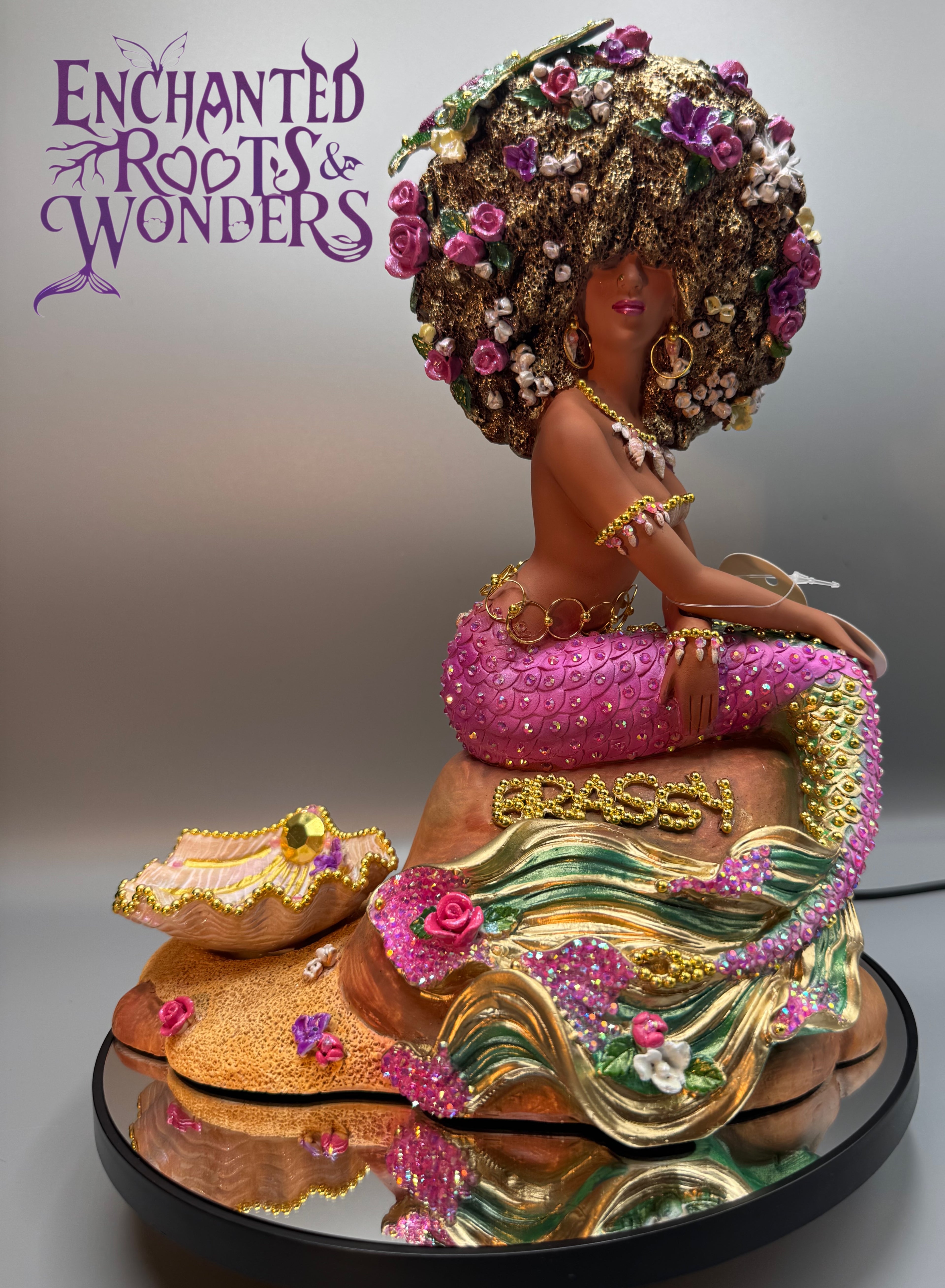 Custom Black mermaid statue with pink rhinestone tail, gold hoop earrings, and Afro-textured hair. Features a bold hoop-style belly chain and gold-accented accessories. Inspired by a New York round-the-way girl with divine Oshún Dynasea energy. One-of-a-kind Brassy by Clover Jené Mermaid.