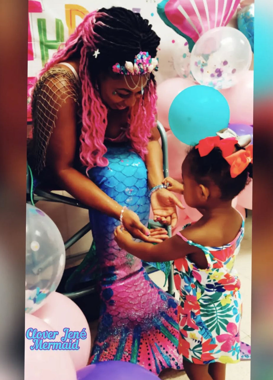 Clover Jené Mermaid, owner of Enchanted Roots & Wonders, posing as a Black mermaid with a little black girl inspiring magic