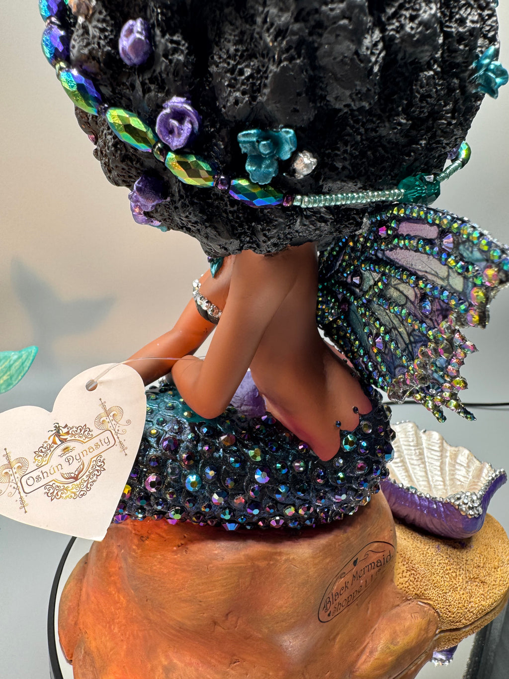Back view of Oil Slick Brassy Black mermaid statue showing rhinestone tail, wings, and Oshún Dynasea product tag