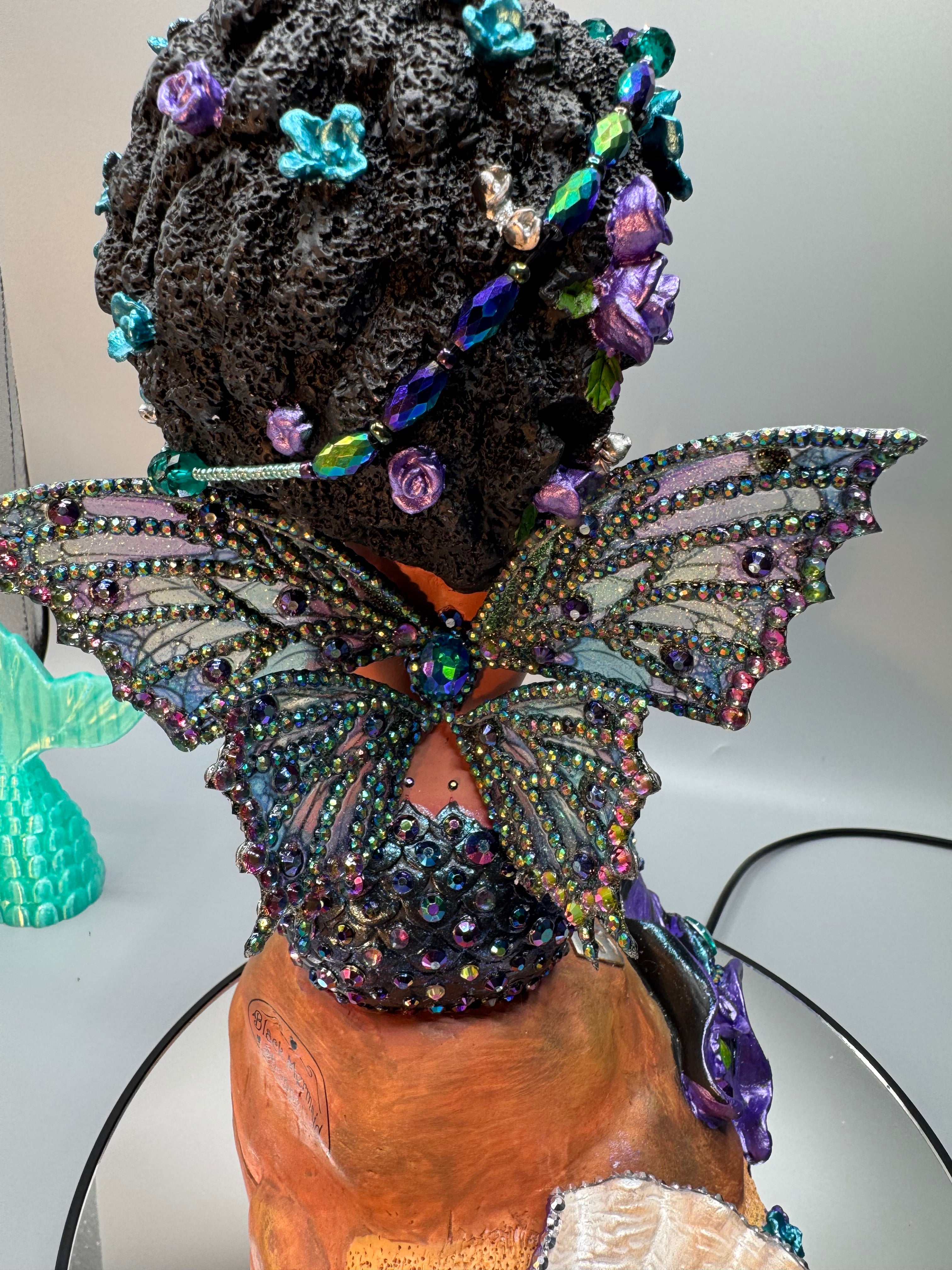 Close-up of Oil Slick Brassy’s rhinestone-embellished wings on a hand-painted Black mermaid statue